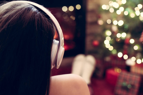 Alone sad woman in headphones sitting and warming at winter evening near fireplace flame and  christmas tree. - Φωτογραφία, εικόνα