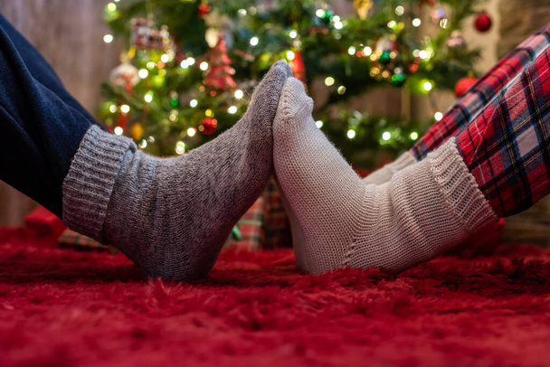 Male and female feet in winter socks touching each other. Man and woman sitting near a Christmas tree with gifts. Concept - Photo, Image