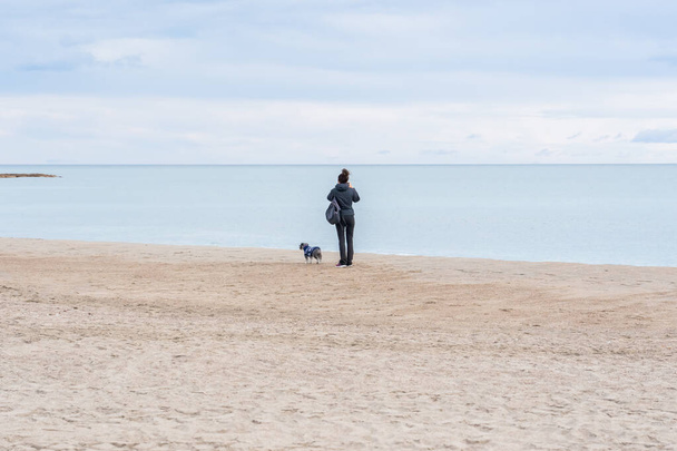 A closeup shot of a female with her dog standing on a beach and observing the beautiful view - Valokuva, kuva