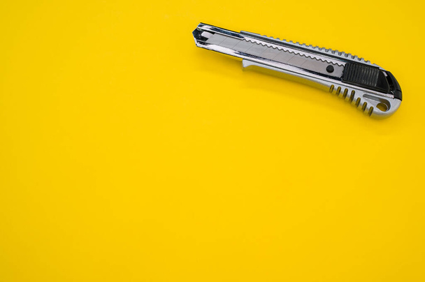 A closeup shot of a cutter blade tool isolated on yellow background. Cutting knife for cardboard - Foto, imagen