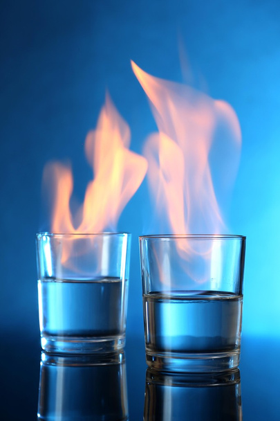 Glasses with burning alcohol on blue background - Фото, зображення