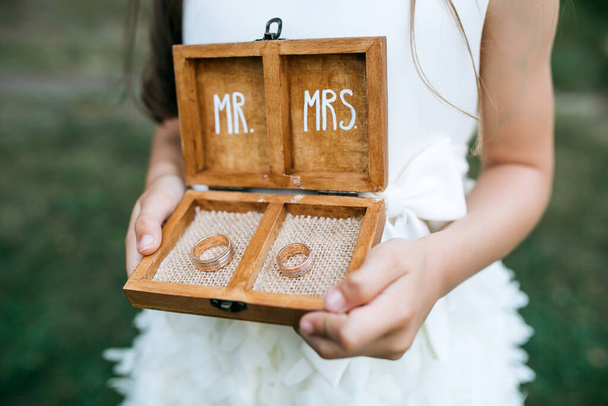 oříznutý záběr holčičky držící dřevěnou krabičku se zlatými snubními prsteny s nápisy pan a paní - Fotografie, Obrázek