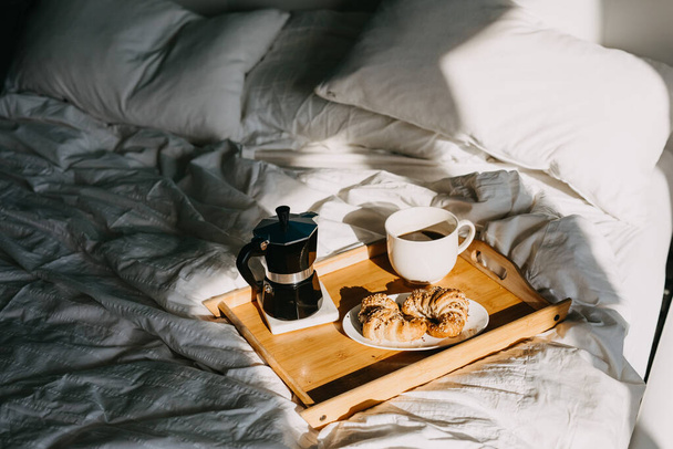 close-up shot of tasty croissants and cup of coffee on wooden tray in bed - Fotoğraf, Görsel