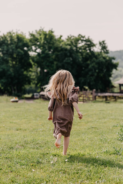 задний вид на стильную маленькую девочку в платье проводит время на открытом воздухе - Фото, изображение
