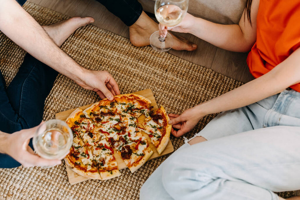 beautiful young couple spending time together at home while eating pizza and drinking wine - Photo, image