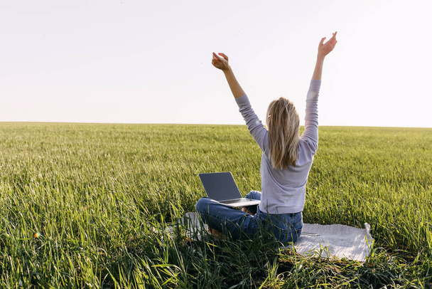 beautiful young woman working with laptop on green field - Photo, Image