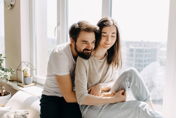 beautiful young couple relaxing on windowsill while spending time together at home - Photo, Image