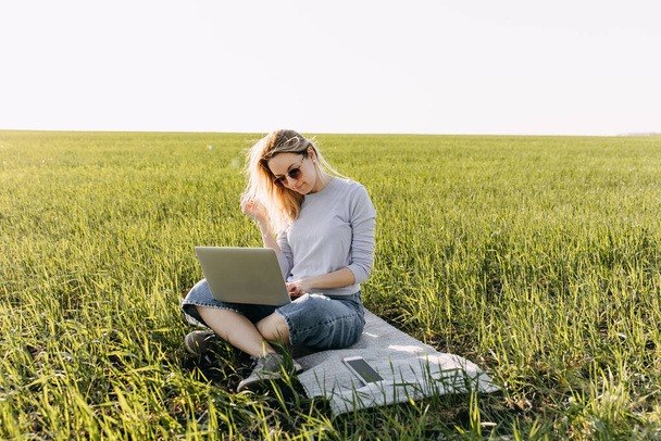 緑の畑でノートパソコンを使って働く美しい若い女性は - 写真・画像