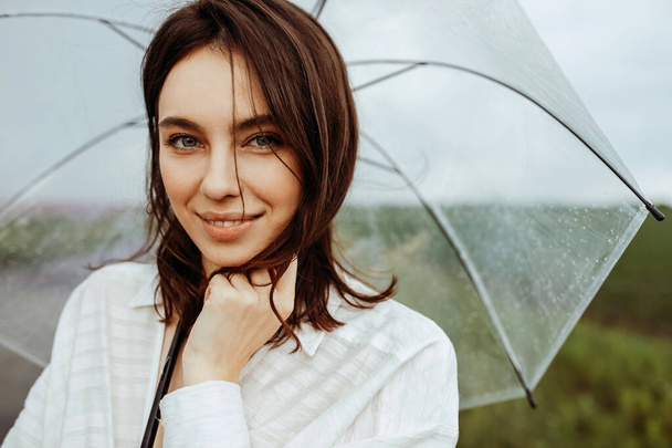 retrato de hermosa mujer joven en vestido con paraguas transparente en prado florido - Foto, imagen