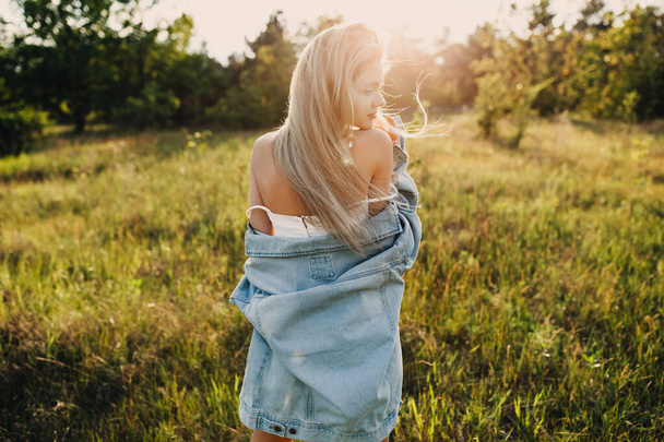 portrait of beautiful young woman in dress and denim jacket on green meadow - Foto, afbeelding