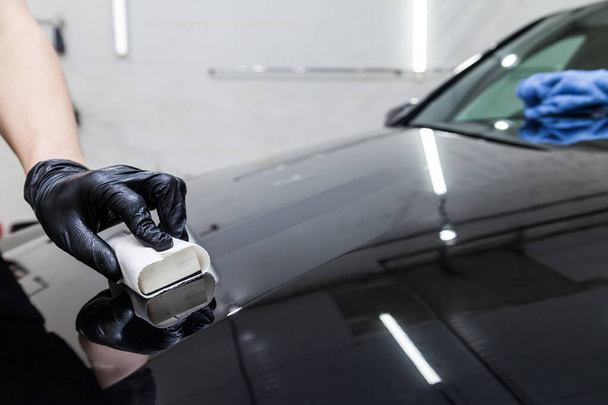 Il processo di applicazione di un rivestimento nano-ceramico sul cofano dell'auto da parte di un lavoratore maschio con una spugna e una speciale composizione chimica per proteggere la vernice sul corpo da graffi, scheggiature e danni. - Foto, immagini