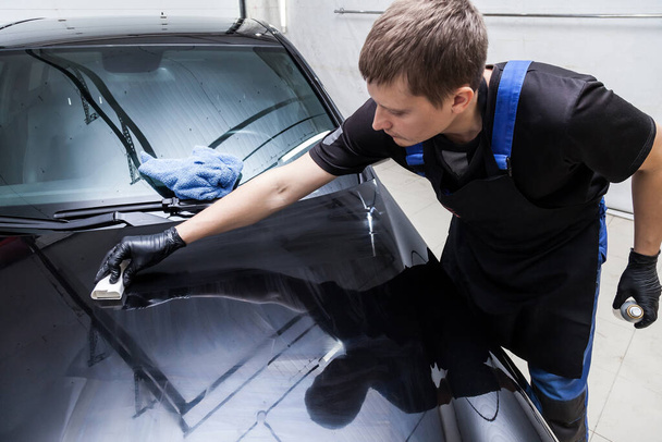 The process of applying a nano-ceramic coating on the car's hood by a male worker with a sponge and special chemical composition to protect the paint on the body from scratches, chips and damage. - Фото, зображення