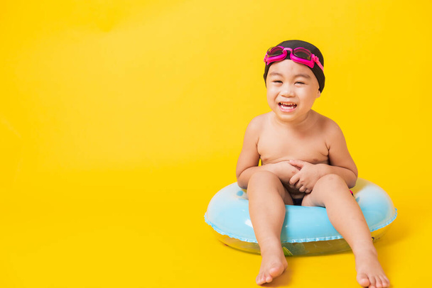 Summer vacation concept, Portrait Asian happy cute little child boy wear goggles, swimsuit hold beach blue inflatable ring, Kid have fun sit in inflatable, studio shot isolated yellow background - Fotografie, Obrázek