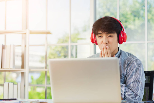 Asian young businessman happiness with red headphones he sitting on desk workplace home office looking to laptop computer monitor, confident handsome man lifestyle smile relax he listens to music - Fotó, kép