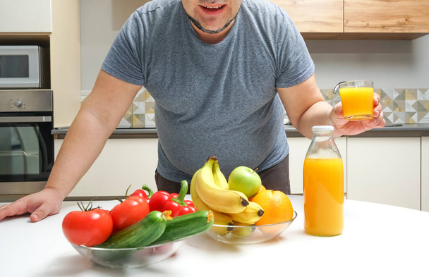 middle aged man making freshly squeezed juice on a table. fruit and vegetable. bottle and glass of orange juice. male pouring orange juice from bottle to glass. - Valokuva, kuva