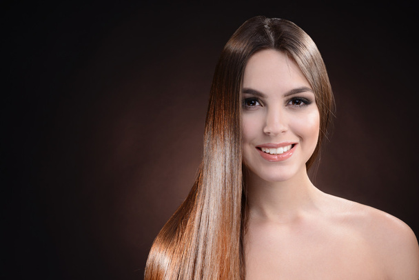 Beautiful young woman with long hair on dark brown background - Valokuva, kuva