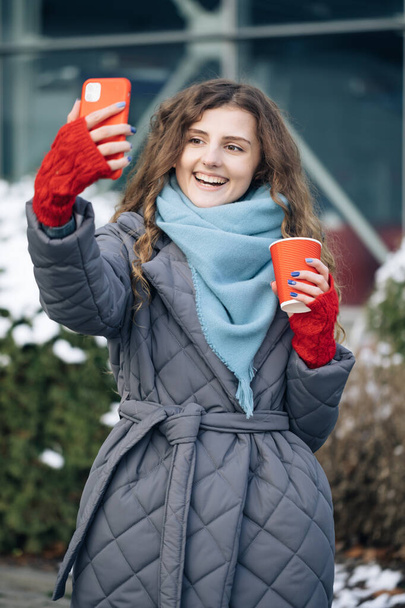 Woman blogger is making video talking for her social page at the street in winter time. Vacation winter outdoor curly girl. Being online, social networks - 写真・画像