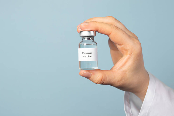 Un medico o un tecnico di laboratorio mantiene il vaccino Prevenar su uno sfondo blu. Vaccinazione contro la pneumocosi, prevenzione della polmonite nei neonati. - Foto, immagini