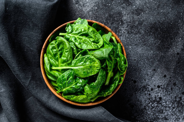 Young raw spinach in a wooden bowl. Black background. Top view. - Photo, Image