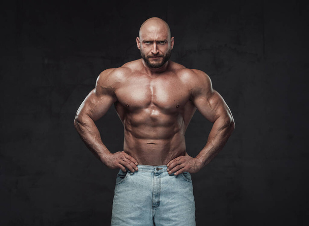 Serious bald bodybuilder posing in dark background with naked torso - Fotó, kép