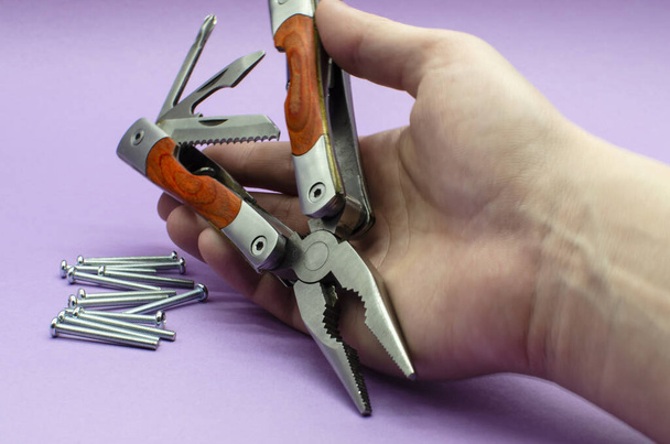 multitool turned into pliers, knife, screwdriver in the hand on violet background, screw. repairing. fix - Photo, Image