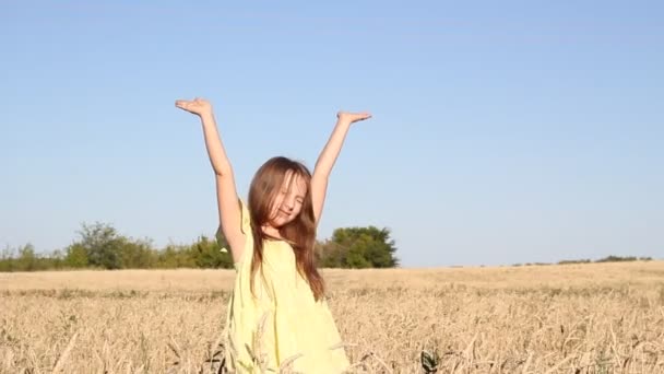 Een meisje met blond haar in een gele jurk loopt in een tarweveld - Video