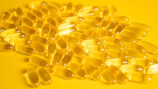 Fish oil capsules with omega 3 on yellow background. Health care concept. Pile of capsules Omega 3 texture - Photo, Image