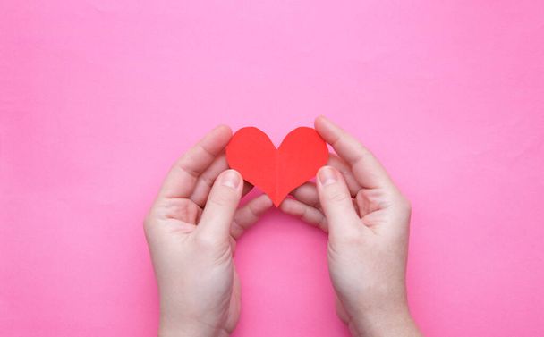paper heart in the palms of a girl on a pink background - Foto, afbeelding