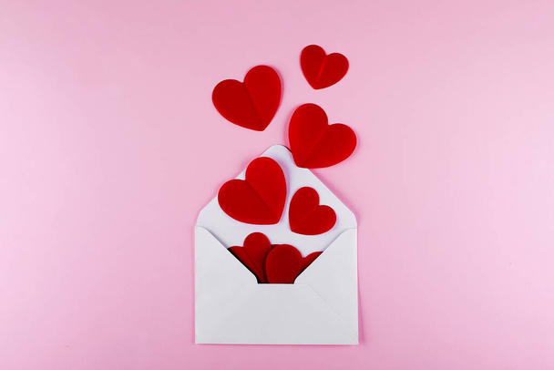 White envelope and red paper hearts on pink background. Valentine's day, love, anniversary concept. - Foto, imagen