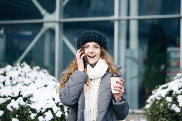 Excited woman winner screaming yes rejoicing success at cellphone. Portrait of young curly woman in winter clothes holding phone celebrate good mobile news surprise bid - Foto, immagini