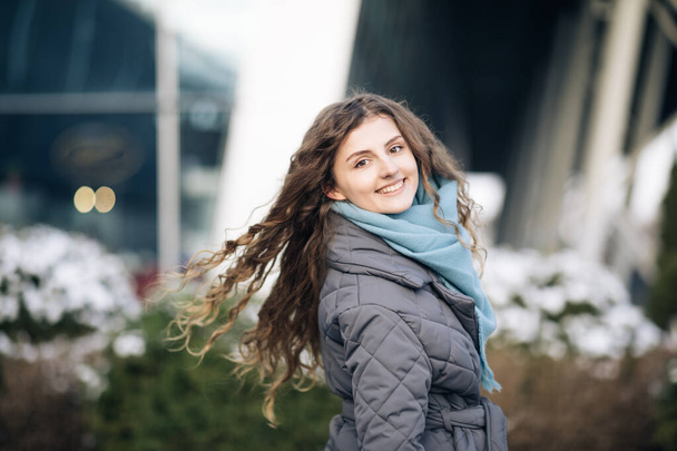 Beautiful caucasian elegant girl with beautiful curly brown hair walks happy in downtown. Happy Young Woman Enjoys Life. Amazing young cheerful curly female model walking on street posing for camera. - Valokuva, kuva