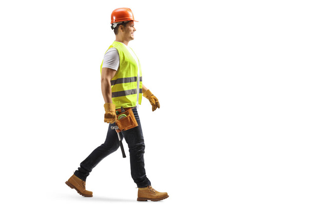 Full length profile shot of a construction worker with a helmet and tool belt walking isolated on white background - Foto, imagen