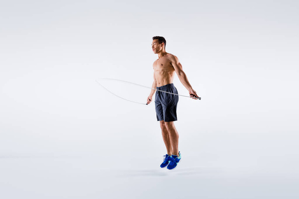 Full length photo of handsone sporty guy using skipping rope to train his perfect body isolated over white color background - Fotó, kép
