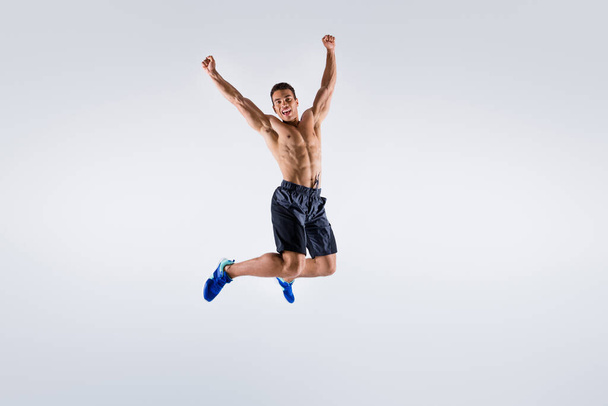 Full size photo of handsome sportsman dark skin guy naked chest jump high up celebrate competition winning raise arms up wear shorts sneakers isolated white color background - Fotoğraf, Görsel