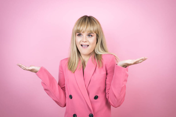 Young caucasian woman over isolated pink background clueless and confused expression with arms and hands raised - Photo, Image