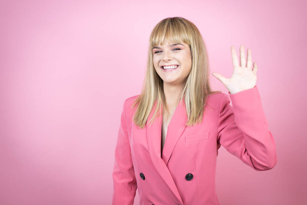 Νεαρή καυκάσια γυναίκα πάνω από απομονωμένο ροζ φόντο δείχνει και δείχνει προς τα πάνω με τα δάχτυλα νούμερο πέντε, ενώ χαμογελά αυτοπεποίθηση και χαρούμενος - Φωτογραφία, εικόνα