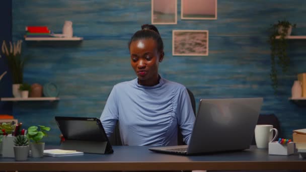 Afrikkalainen nainen käyttää kannettavaa tietokonetta ja tablettia samaan aikaan ylitöitä - Materiaali, video
