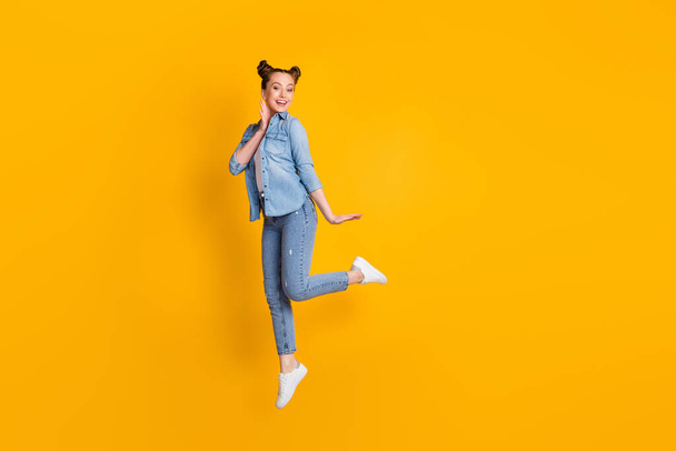 Full length profile photo of attractive funny lady jump high up good mood sunny summer day weekend vacation wear casual denim shirt sneakers isolated yellow color background - Fotografie, Obrázek