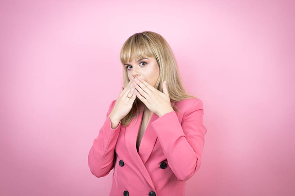 Joven mujer caucásica sobre fondo rosa aislado con las manos sobre la boca y sorprendida - Foto, Imagen