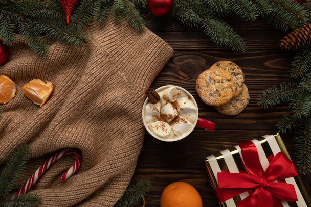На столе украшенном рождественским декором, есть чашка горячего шоколада и праздничное печенье. - Фото, изображение