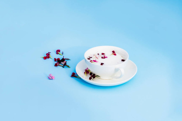 White Cup with vegan milk and flowers on a blue background. Concept of vegetarian drinks and food, herbal teas, beauty and health, Spa. - 写真・画像