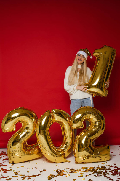 vonzó nő kényelmes ruhákban mosolyog közelében nagy arany léggömbök számok 2021 - Fotó, kép