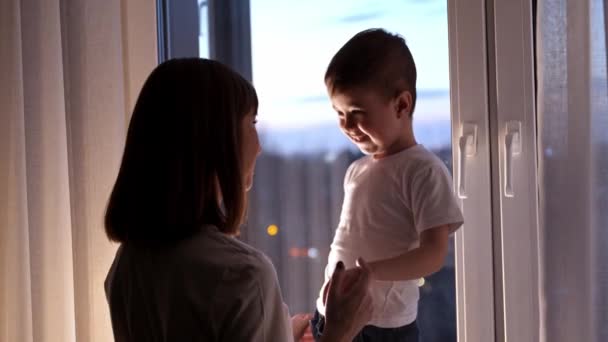Een lachende jongen die op de vensterbank stond en met haar moeder praatte. - Video