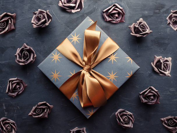 Blue gift box with gold ribbon bow and violet artificial roses on blue background. Overhead shot. - Photo, Image