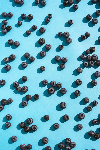 Many Blueberries on blue background. Closeup flat lay pattern in sunlight. Vegan and vegetarian concept. Macro texture of blueberry berries. Organic raw food natural wallpaper texture. - 写真・画像