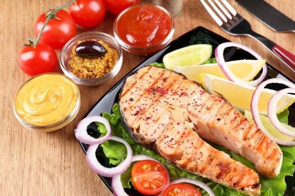 Tasty grilled salmon with lemon and vegetables, on wooden table  - Photo, Image