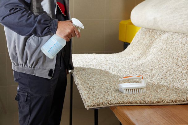 Man Spray detergent na szarym dywanie, aby usunąć Stain w profesjonalnej usługi sprzątania  - Zdjęcie, obraz
