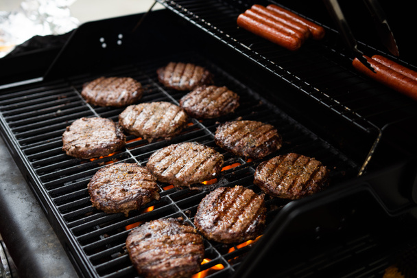 Hamburgers en hotdogs koken op vlam verkoold achtertuin grill - Foto, afbeelding