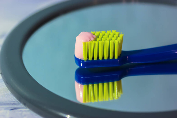 Синя зубна щітка з зеленою щетиною крупним планом відбивається у дзеркальній, рожевій зубній пасті. Гігієна ротової порожнини та засоби для догляду за зубами щодня
 - Фото, зображення