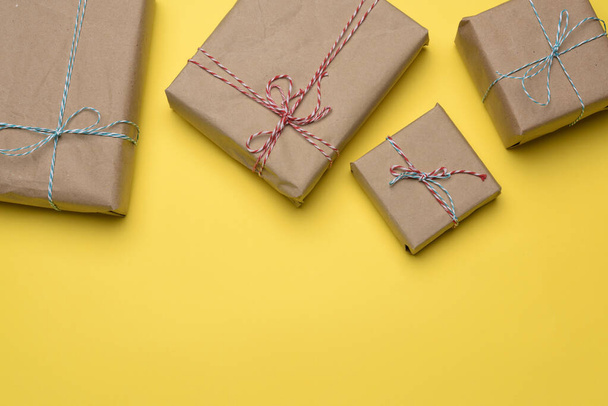 boîte enveloppée dans du papier brun et attachée avec une corde, cadeau sur fond jaune, vue du dessus, espace de copie - Photo, image